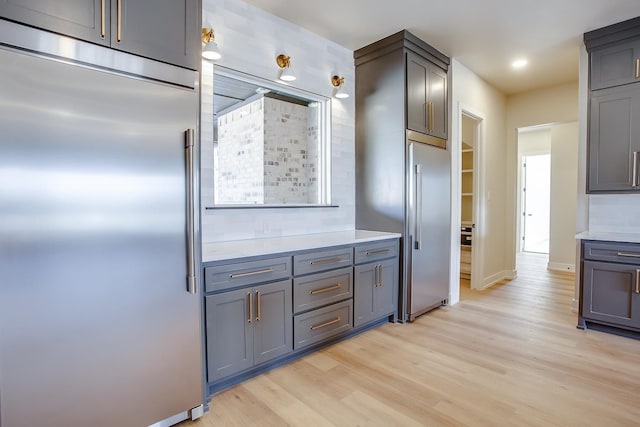 kitchen with built in fridge, gray cabinets, light countertops, light wood-style flooring, and baseboards