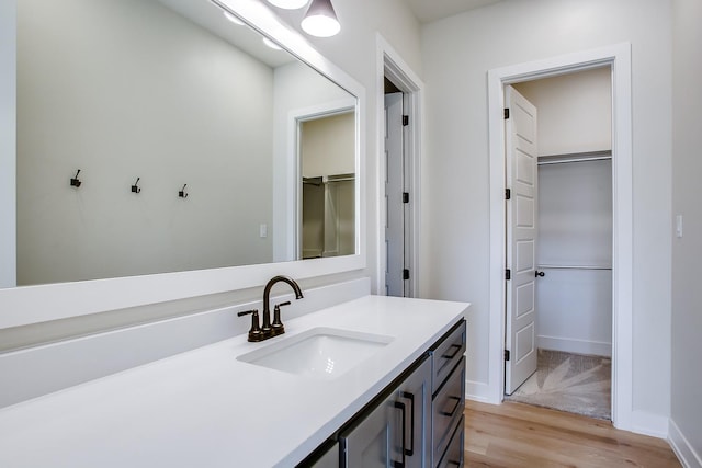 bathroom featuring baseboards, a walk in closet, wood finished floors, and vanity