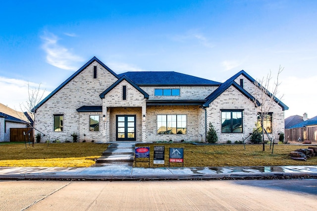 view of front facade with french doors, brick siding, fence, and a front lawn