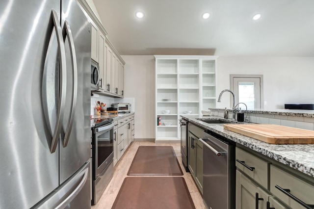 kitchen with sink, gray cabinetry, light stone counters, appliances with stainless steel finishes, and decorative backsplash