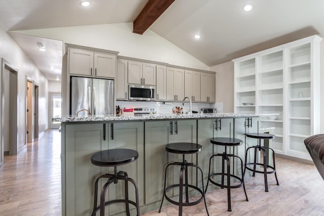 kitchen featuring vaulted ceiling with beams, gray cabinetry, a kitchen breakfast bar, stainless steel appliances, and a center island with sink