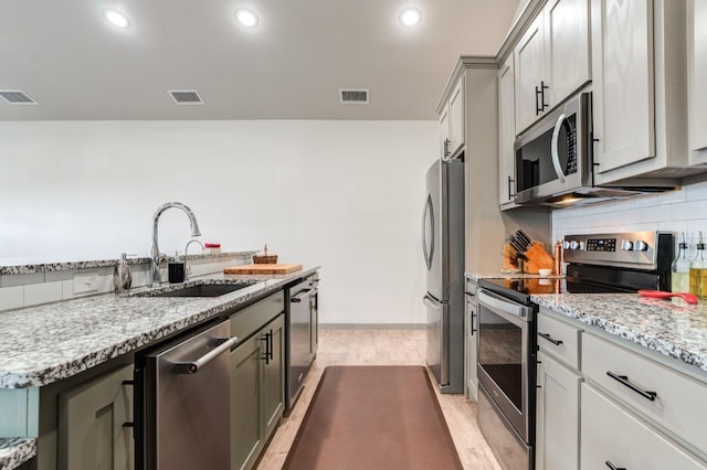 kitchen with sink, light stone counters, gray cabinets, stainless steel appliances, and decorative backsplash