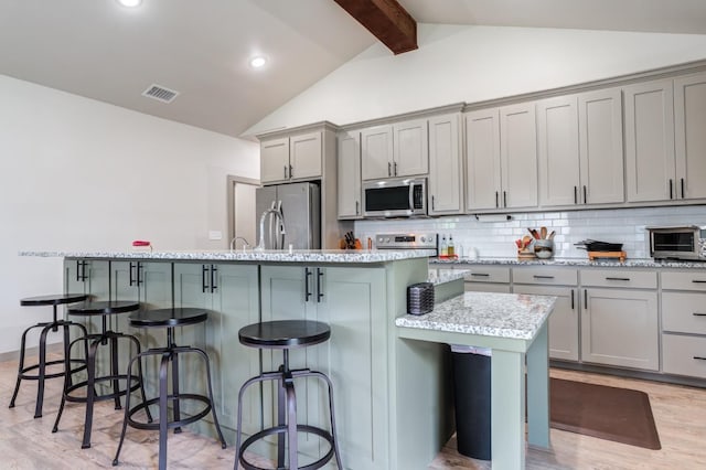 kitchen with gray cabinets, a center island with sink, stainless steel appliances, a kitchen bar, and decorative backsplash