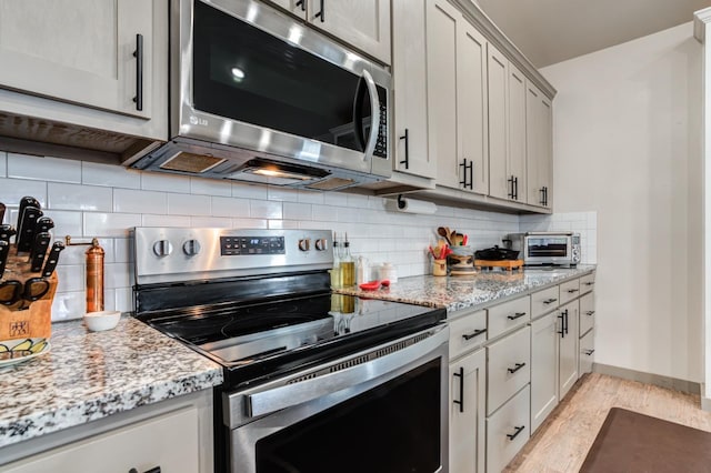 kitchen with light stone countertops, appliances with stainless steel finishes, backsplash, and light hardwood / wood-style flooring