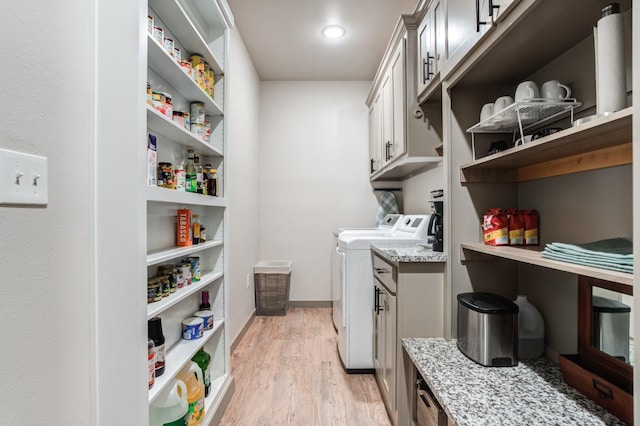 clothes washing area featuring separate washer and dryer, light hardwood / wood-style flooring, and cabinets