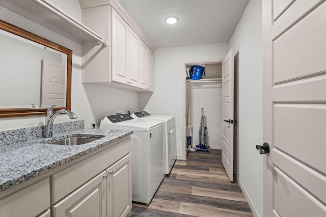 clothes washing area with dark wood-style flooring, washing machine and clothes dryer, cabinet space, a sink, and baseboards