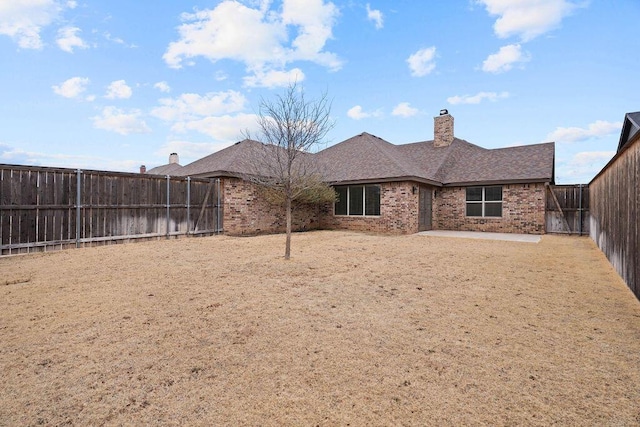 back of house with a patio, a fenced backyard, brick siding, roof with shingles, and a chimney