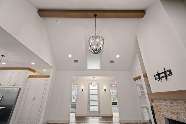 entrance foyer with a chandelier, high vaulted ceiling, a stone fireplace, and visible vents