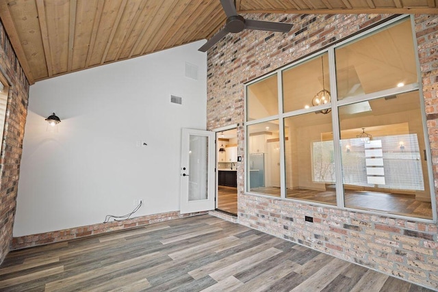 empty room with ceiling fan with notable chandelier, brick wall, wood finished floors, visible vents, and wood ceiling