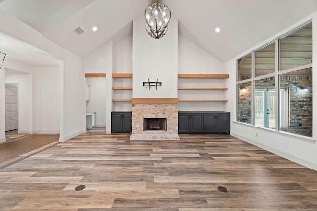 unfurnished living room featuring built in shelves, visible vents, a fireplace with raised hearth, and wood finished floors