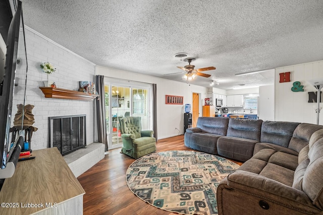 4411 58th St, Lubbock, TX 79414 - living room with a textured ceiling, wood finished floors, ceiling fan, crown molding, and a brick fireplace
