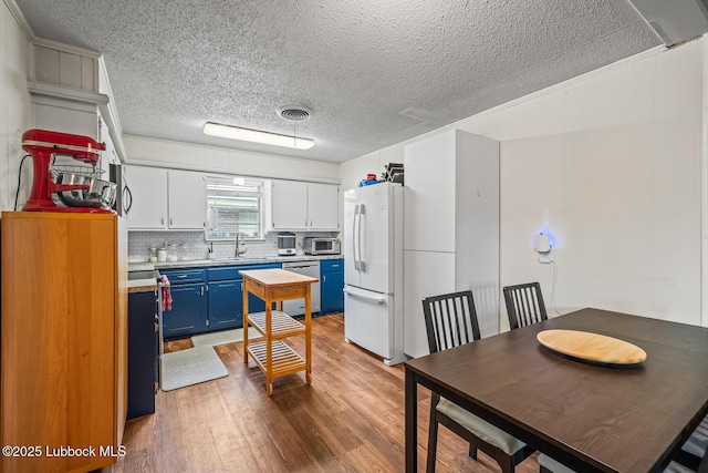 4411 58th St, Lubbock, TX 79414 - kitchen with blue cabinetry, freestanding refrigerator, dishwasher, light countertops, and wood finished floors