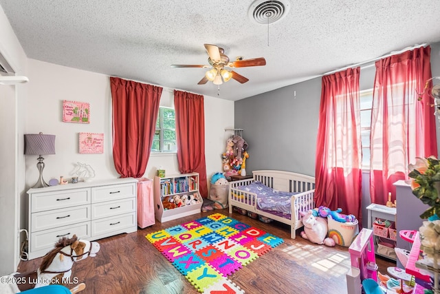 4411 58th St, Lubbock, TX 79414 - bedroom with wood finished floors, a textured ceiling, a nursery area, and a ceiling fan