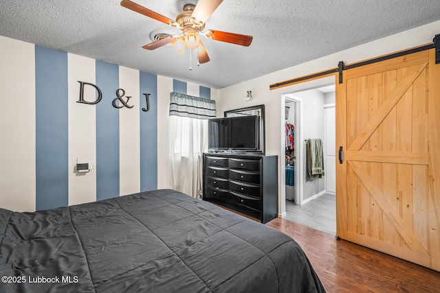 4411 58th St, Lubbock, TX 79414 - bedroom featuring a barn door, a textured ceiling, wood finished floors, a ceiling fan, and a walk in closet