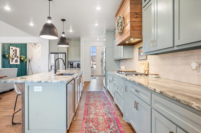 kitchen featuring decorative light fixtures, an island with sink, sink, custom exhaust hood, and stainless steel appliances