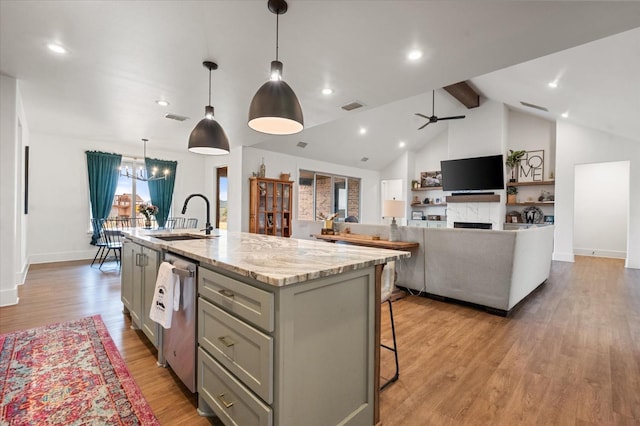 kitchen with sink, a kitchen island with sink, gray cabinetry, light stone counters, and decorative light fixtures