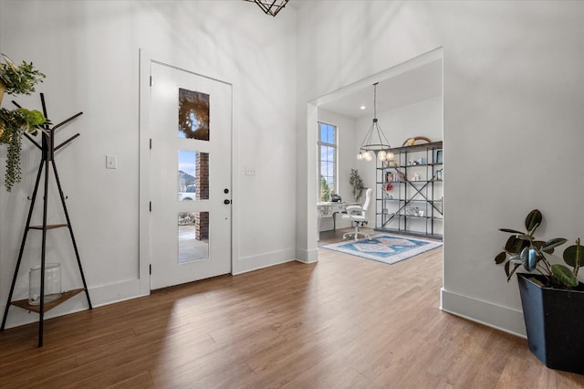 entryway with hardwood / wood-style flooring, a towering ceiling, and an inviting chandelier