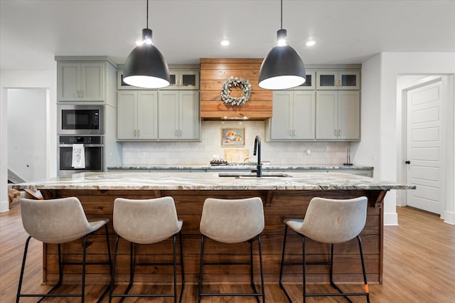 kitchen featuring sink, light stone countertops, a center island with sink, built in microwave, and oven