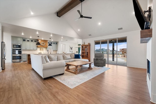 living room featuring beamed ceiling, ceiling fan with notable chandelier, high vaulted ceiling, and light wood-type flooring