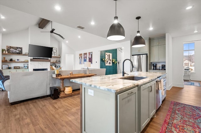 kitchen featuring pendant lighting, gray cabinetry, stainless steel appliances, light stone counters, and an island with sink