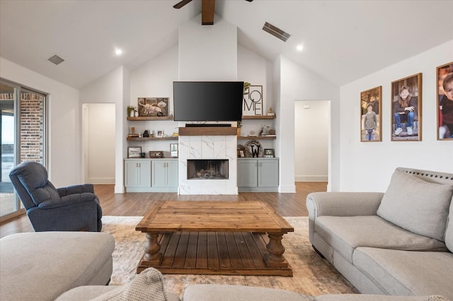 living room with beamed ceiling, high vaulted ceiling, a premium fireplace, and light hardwood / wood-style floors