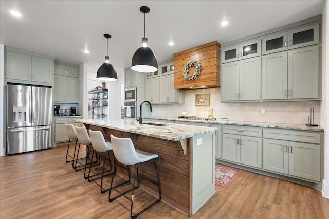 kitchen with sink, decorative light fixtures, stainless steel appliances, light stone countertops, and a kitchen island with sink