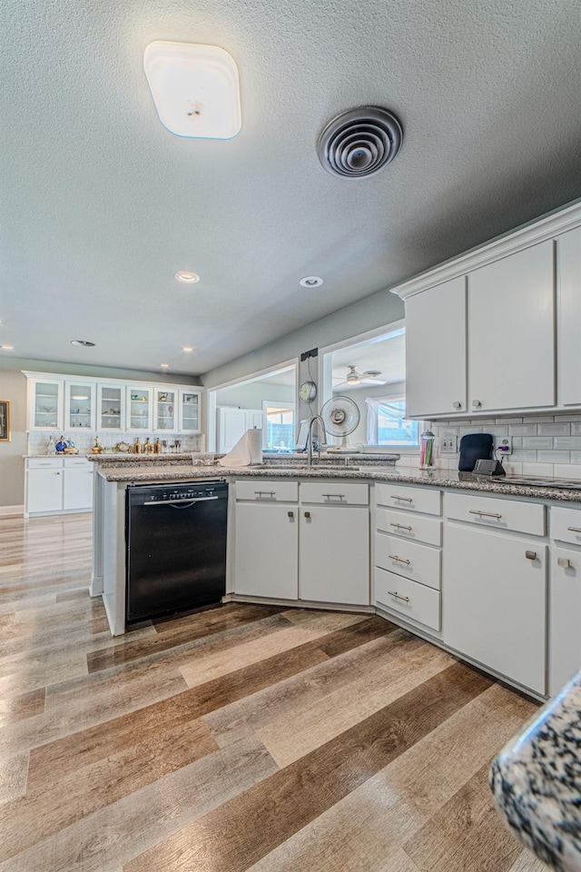 kitchen with white cabinets, decorative backsplash, light hardwood / wood-style flooring, and black dishwasher