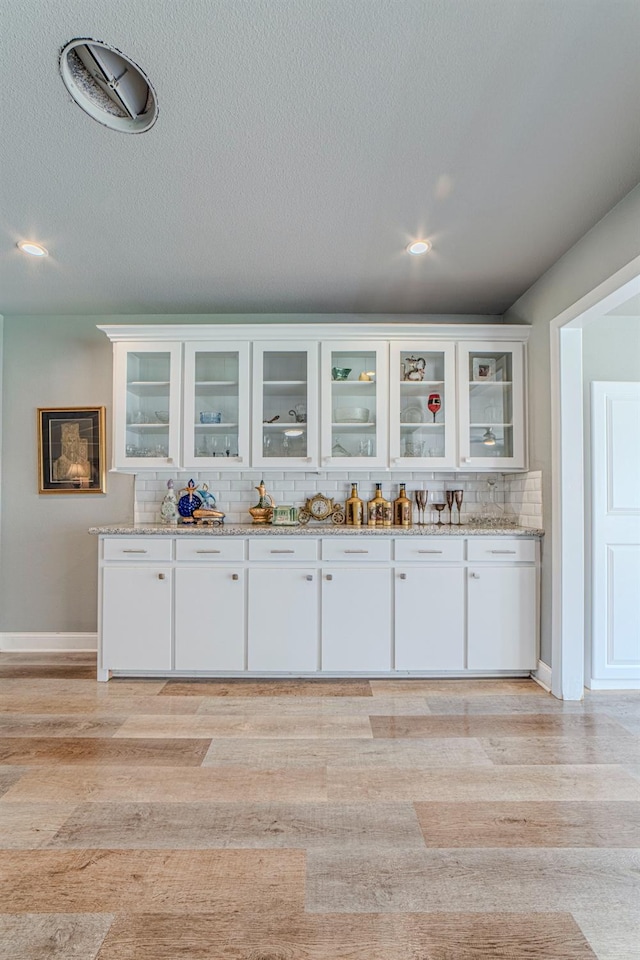 bar with white cabinetry, light stone counters, tasteful backsplash, a textured ceiling, and light wood-type flooring