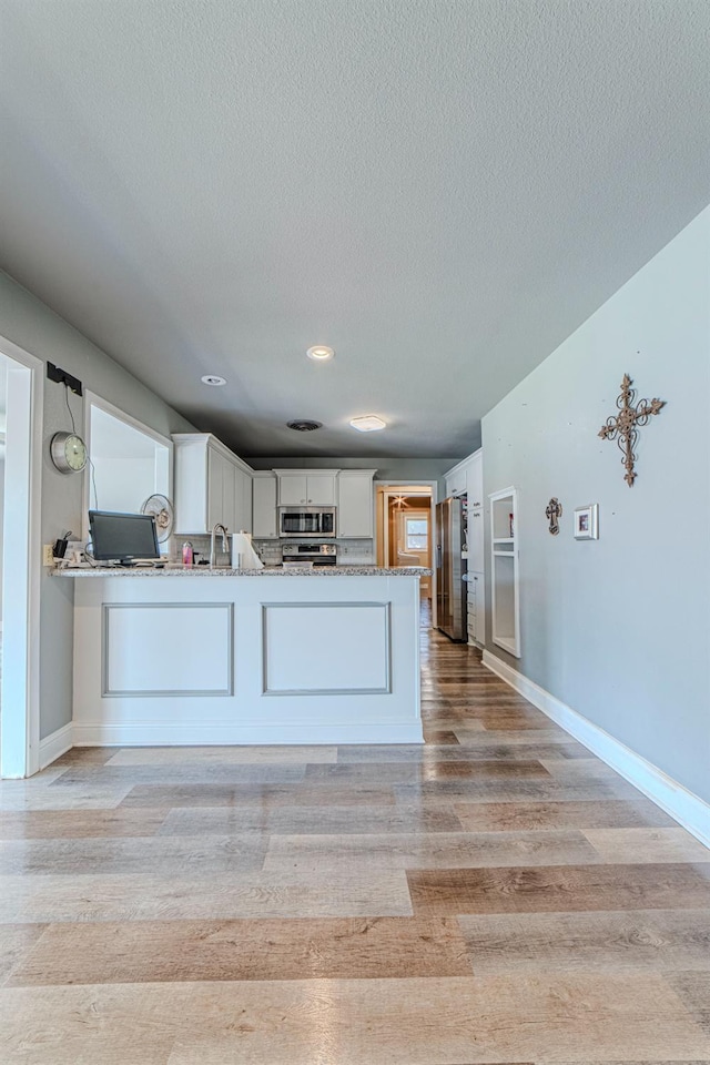 kitchen with appliances with stainless steel finishes, white cabinetry, kitchen peninsula, light stone countertops, and light wood-type flooring