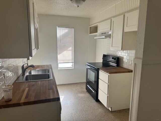 kitchen featuring wood counters, black electric range oven, sink, white cabinets, and a textured ceiling