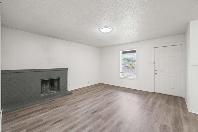 unfurnished living room with a brick fireplace, a textured ceiling, and light wood-type flooring