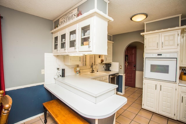 kitchen with dishwasher, a sink, arched walkways, white oven, and a textured ceiling