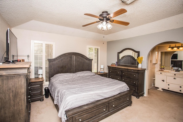bedroom featuring light carpet, arched walkways, a textured ceiling, and ceiling fan