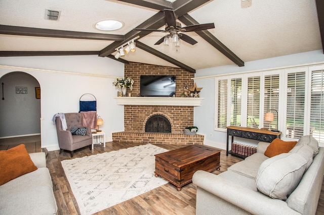 living area featuring vaulted ceiling with beams, wood finished floors, visible vents, and ceiling fan