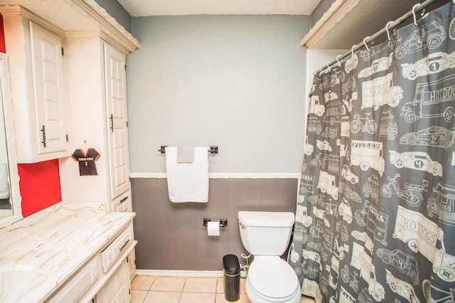 bathroom featuring vanity, curtained shower, a wainscoted wall, toilet, and tile patterned flooring