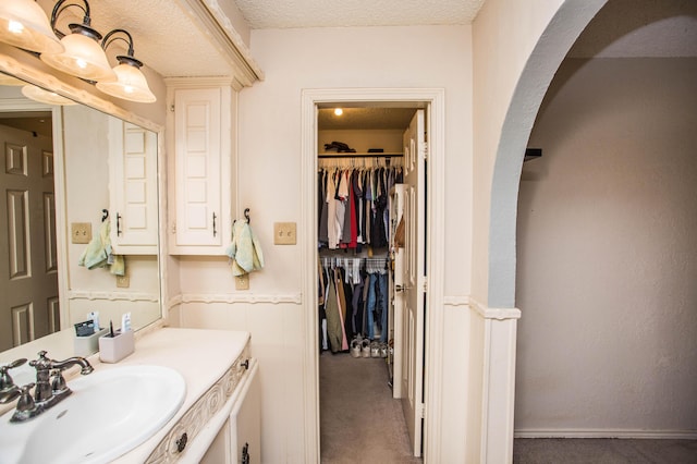 bathroom featuring wainscoting, vanity, a spacious closet, and a textured ceiling