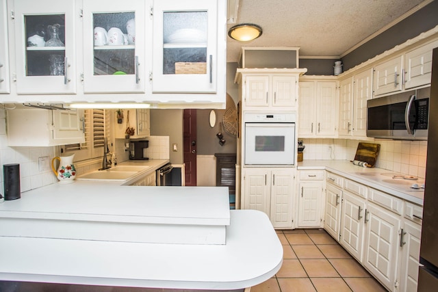 kitchen with stainless steel appliances, light countertops, glass insert cabinets, and tasteful backsplash