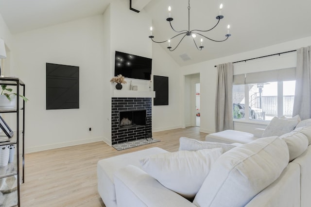 living room with light wood-type flooring, high vaulted ceiling, a brick fireplace, and a notable chandelier