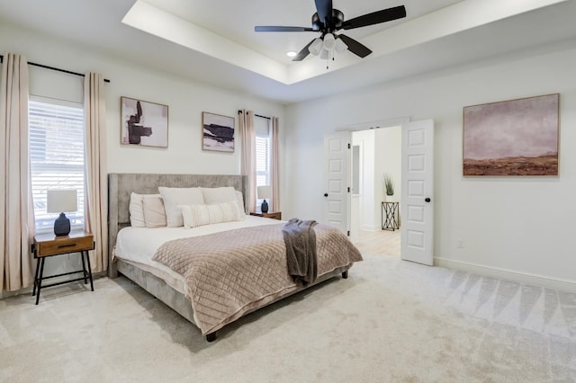 bedroom featuring ceiling fan, light colored carpet, and a tray ceiling