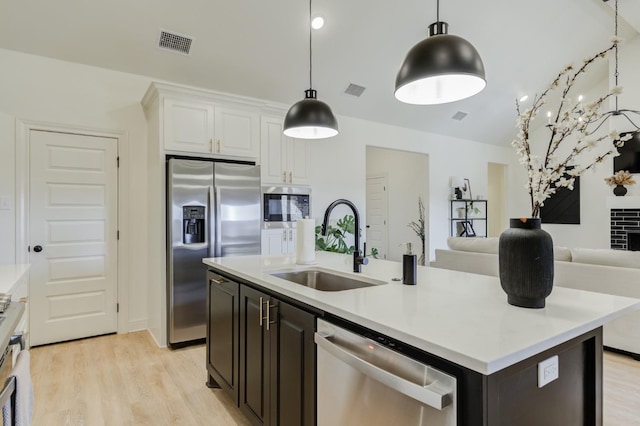 kitchen featuring sink, appliances with stainless steel finishes, white cabinetry, a kitchen island with sink, and light wood-type flooring