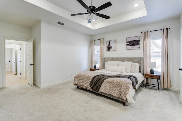 bedroom featuring a raised ceiling, light colored carpet, and ceiling fan