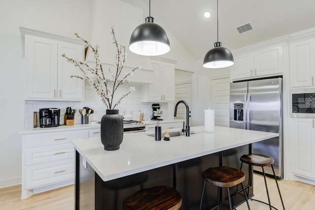 kitchen with sink, an island with sink, white cabinets, and stainless steel refrigerator with ice dispenser