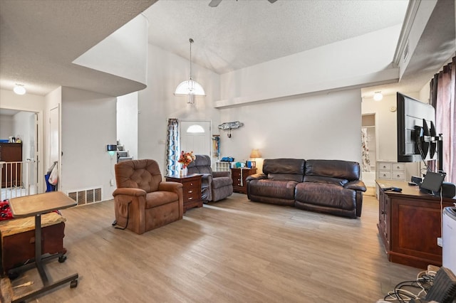 living room with ceiling fan, high vaulted ceiling, a textured ceiling, and light wood-type flooring