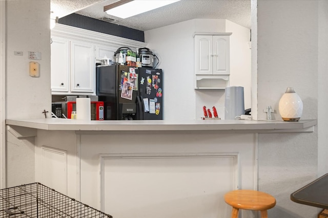 kitchen with white cabinetry, kitchen peninsula, a textured ceiling, and black fridge