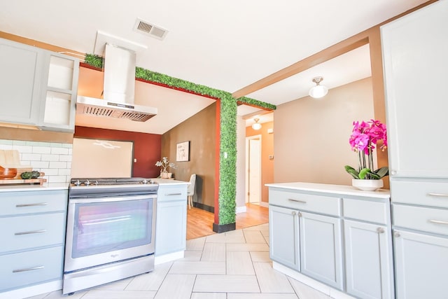 kitchen with stainless steel stove, island range hood, decorative backsplash, and white cabinets