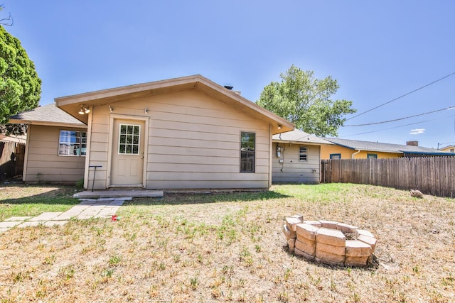 back of property with an outdoor fire pit and a lawn