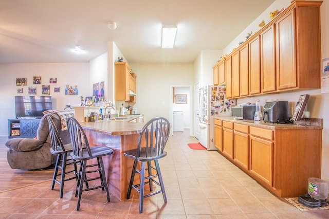 kitchen featuring white refrigerator, sink, a breakfast bar area, and light tile patterned floors