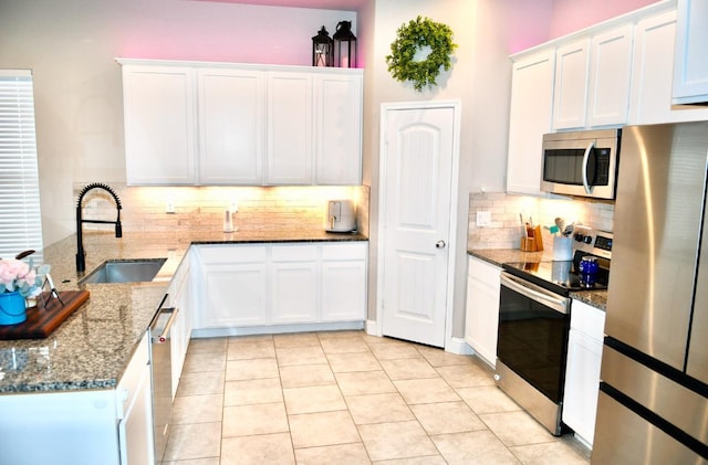 kitchen featuring white cabinetry, stainless steel appliances, sink, and dark stone counters