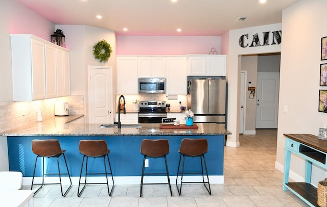 kitchen with sink, a breakfast bar, stainless steel appliances, white cabinets, and dark stone counters