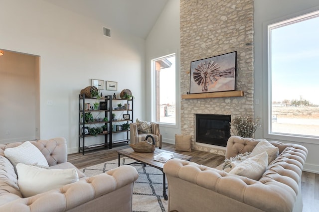 living room with a stone fireplace, high vaulted ceiling, and light wood-type flooring